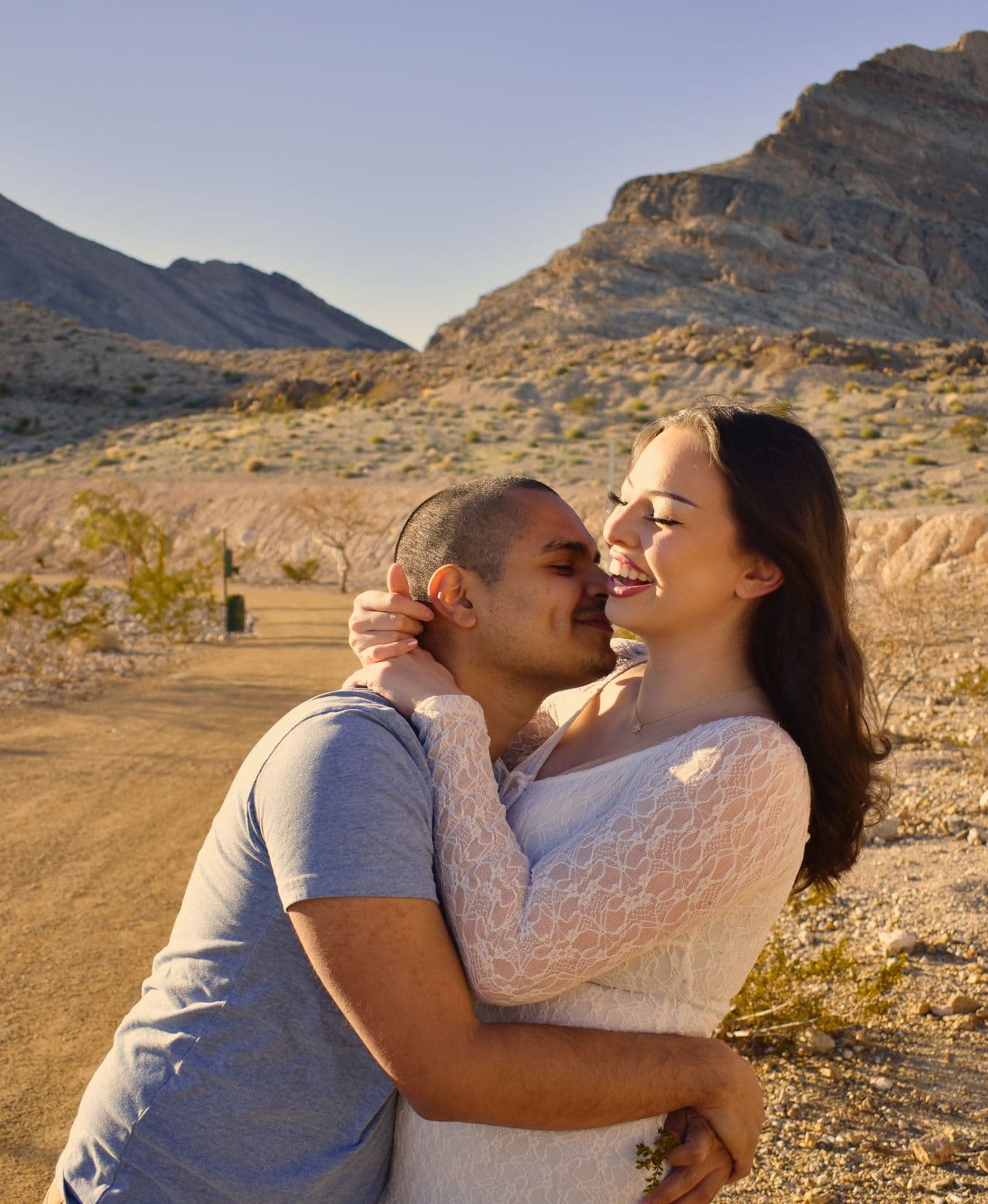 A couple embracing on a desert road with a mountain ridge behind them near Las Vegas, NV