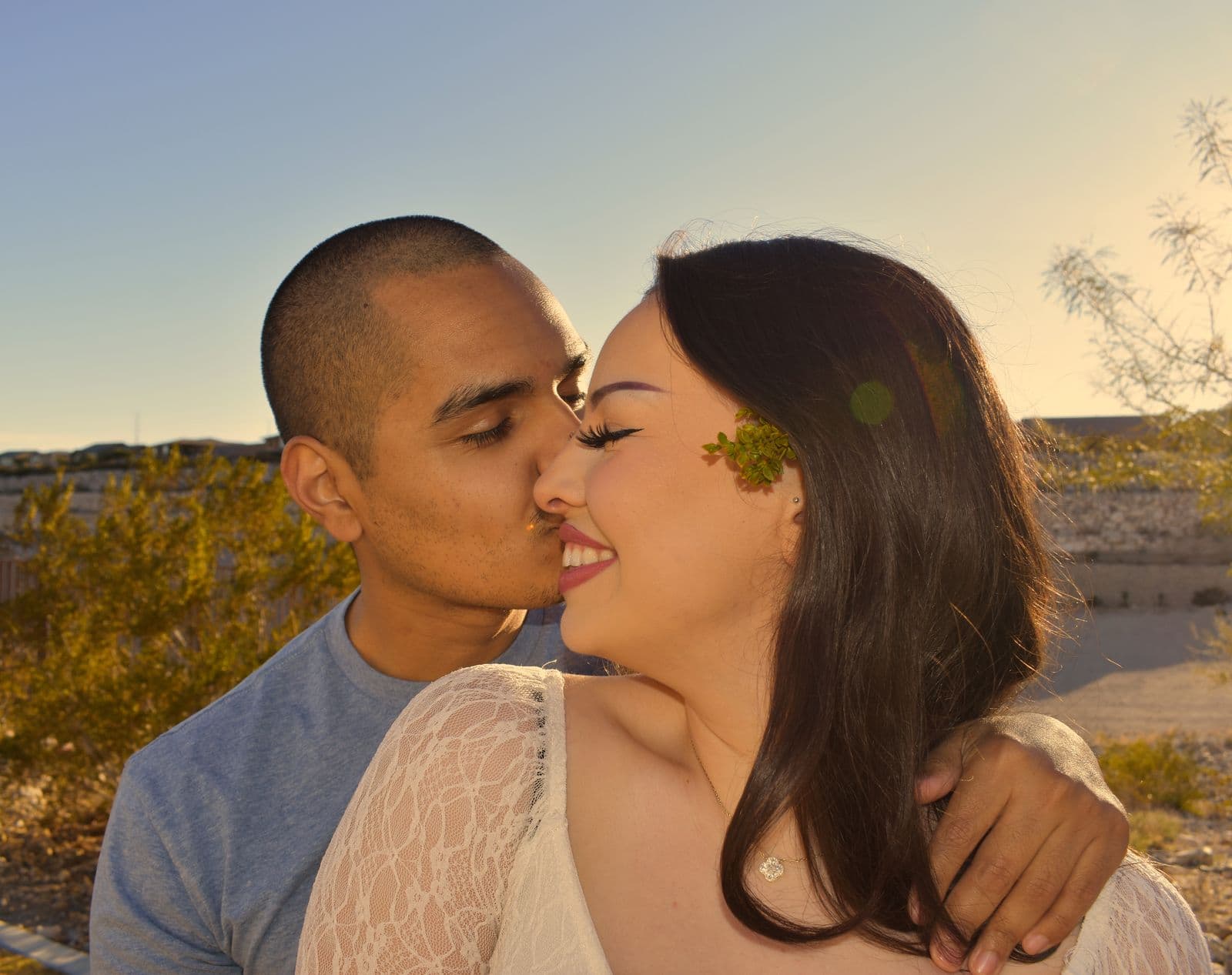 A couple kissing with a sprig of yellow desert bloom between them near Las Vegas, NV