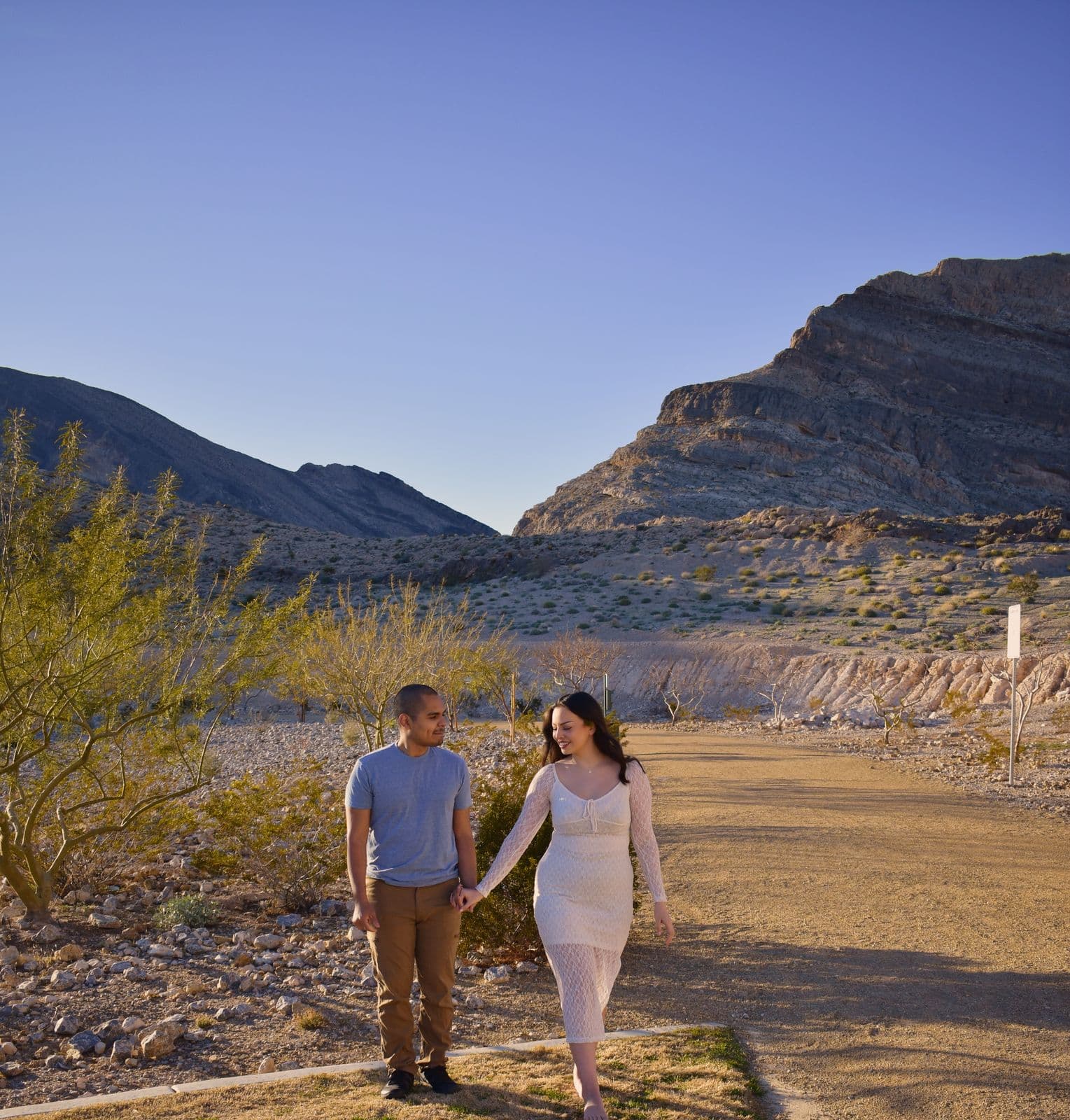 A couple walking a dirt path hand in hand below a desert mountain near Las Vegas, NV