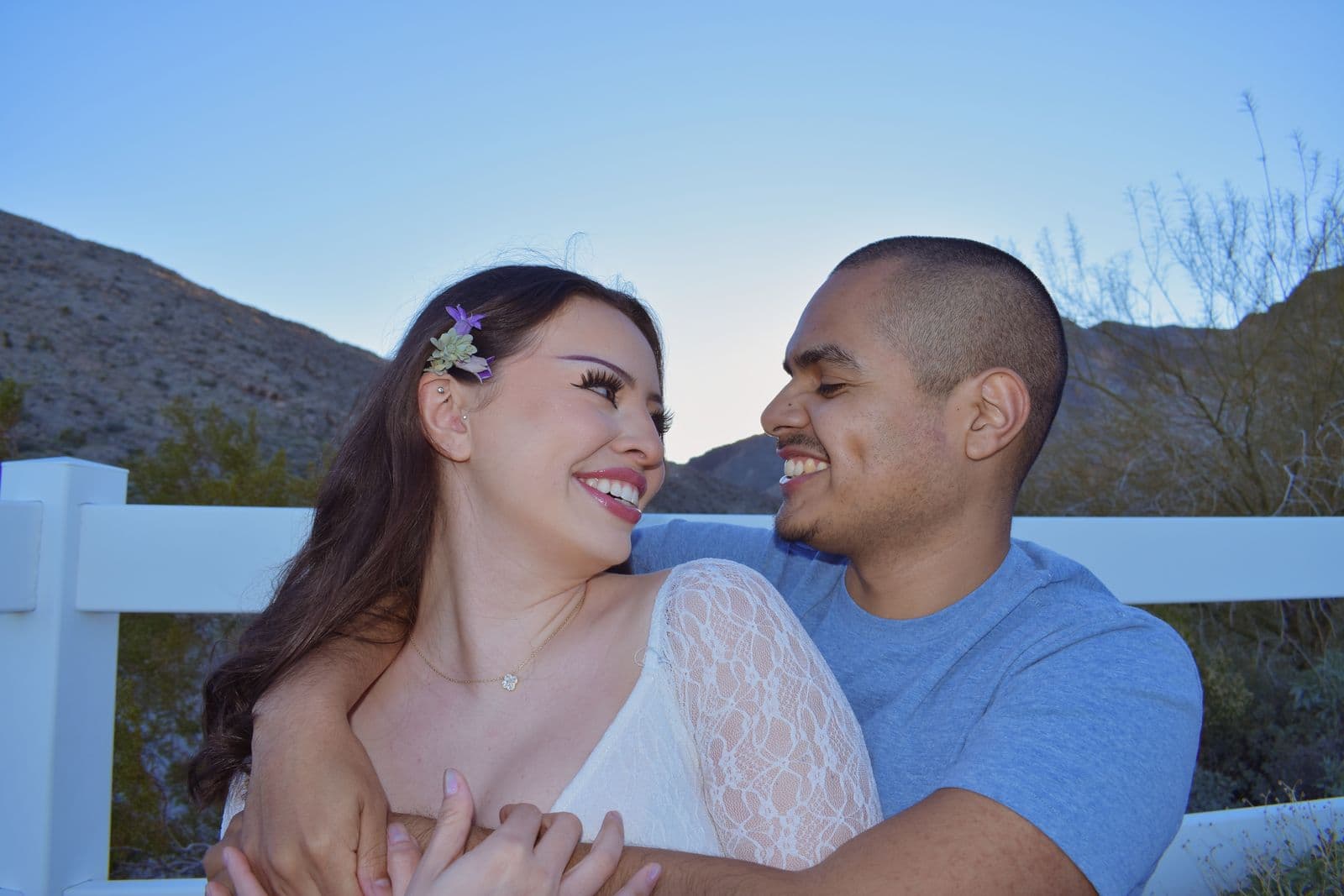 A couple leaning on a white ranch fence and laughing together during a session near Las Vegas, NV