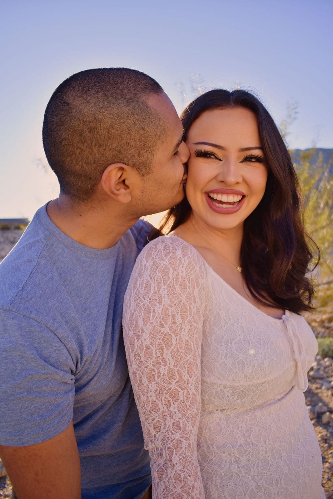 A man kissing his partner's cheek as she smiles at the camera during a desert couples session near Las Vegas, NV