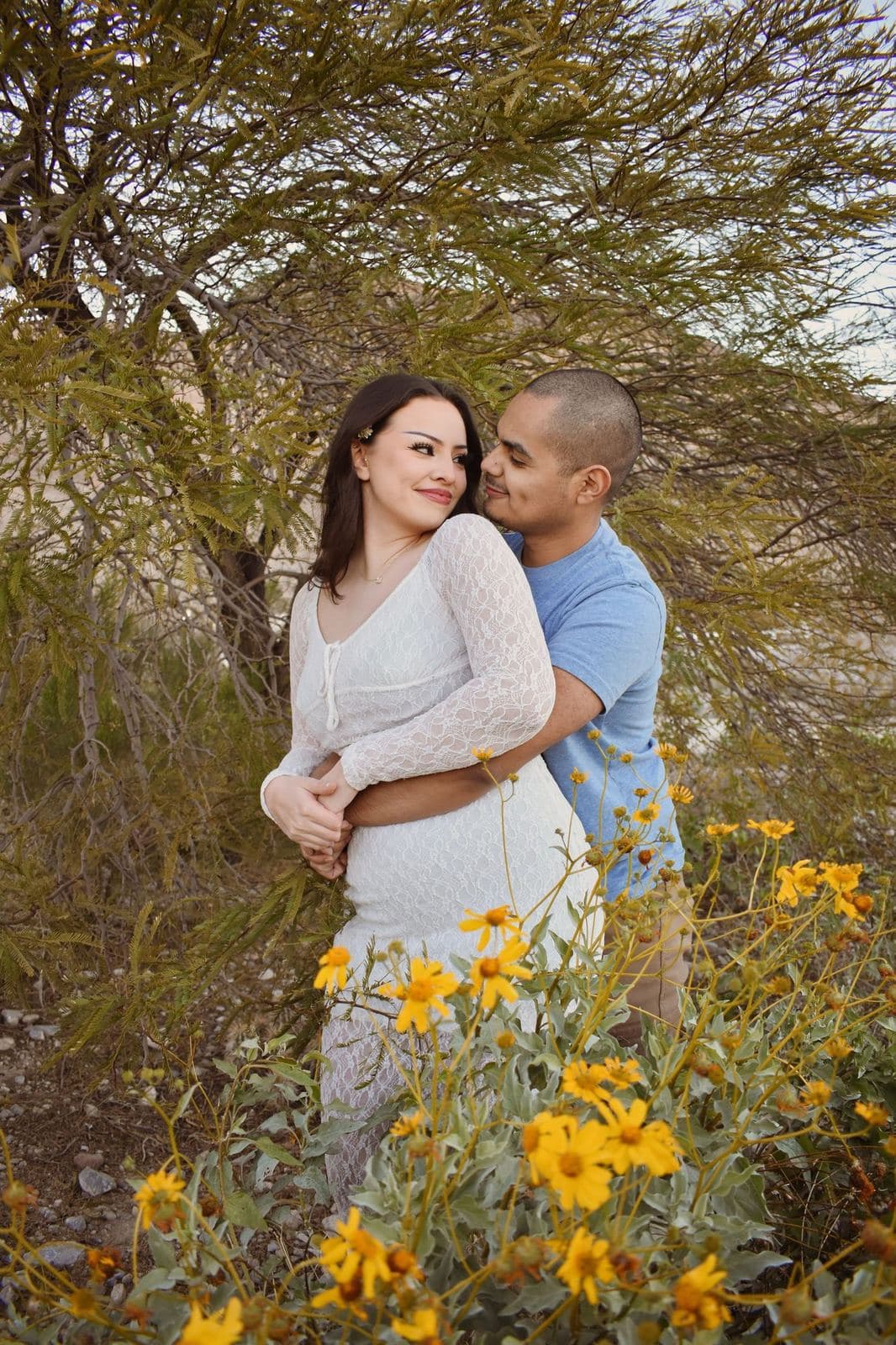 A couple embracing beneath a desert tree with yellow wildflowers blooming in the foreground near Las Vegas, NV