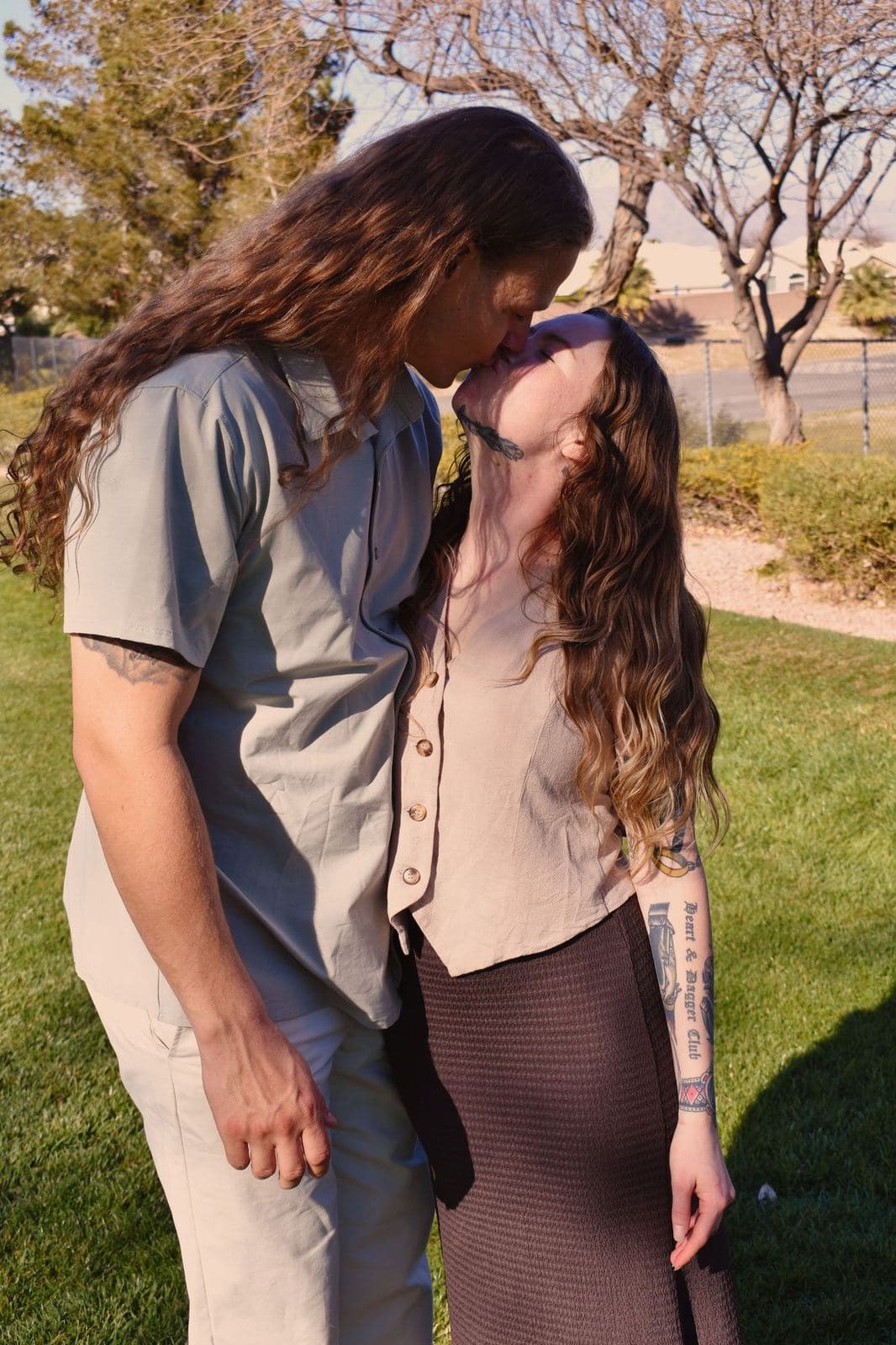 A couple kissing on a park lawn beneath bare spring trees in Las Vegas, NV