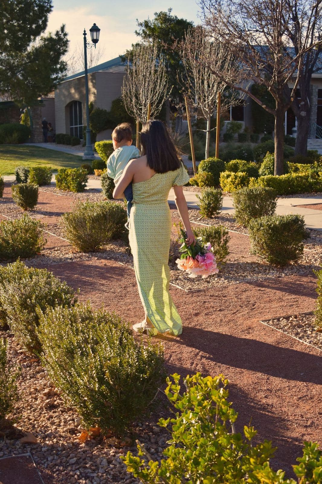 A mother carrying her toddler along a landscaped garden path at sunset in Las Vegas, NV