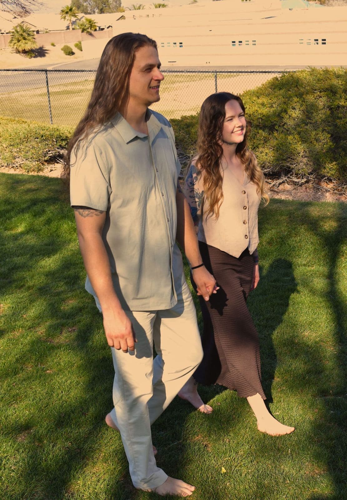 A couple walking barefoot together across a sunlit park lawn in Las Vegas, NV