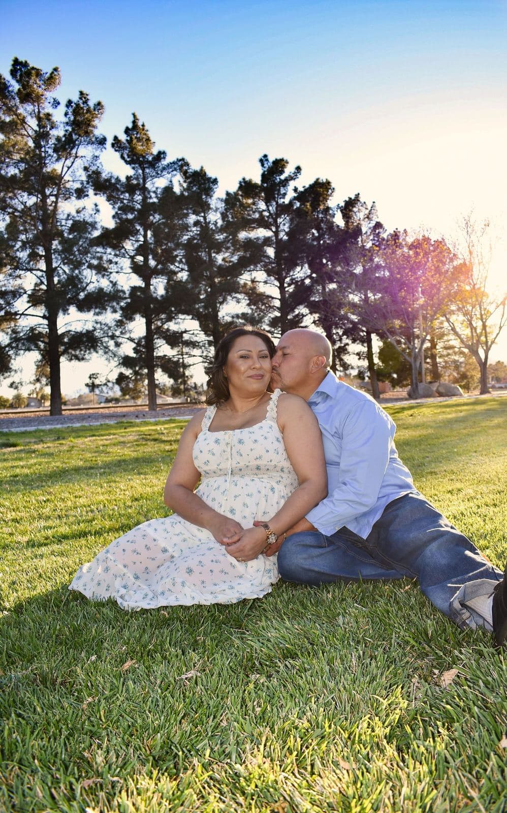 A couple sitting on the grass with their baby at sunset, tall pines behind them, in Las Vegas, NV