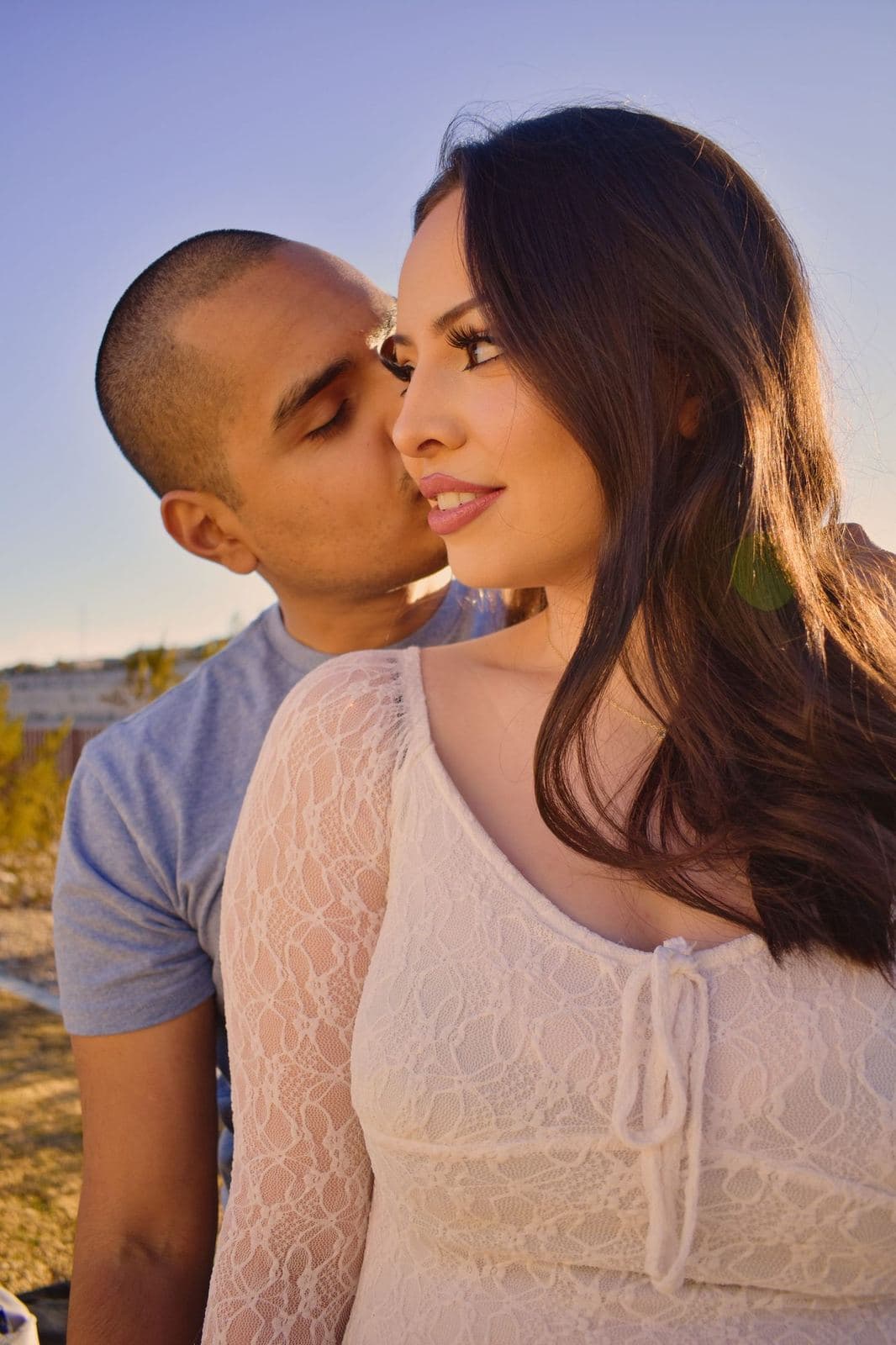 A man kissing his partner's cheek from behind at sunset during a desert couples session near Las Vegas, NV