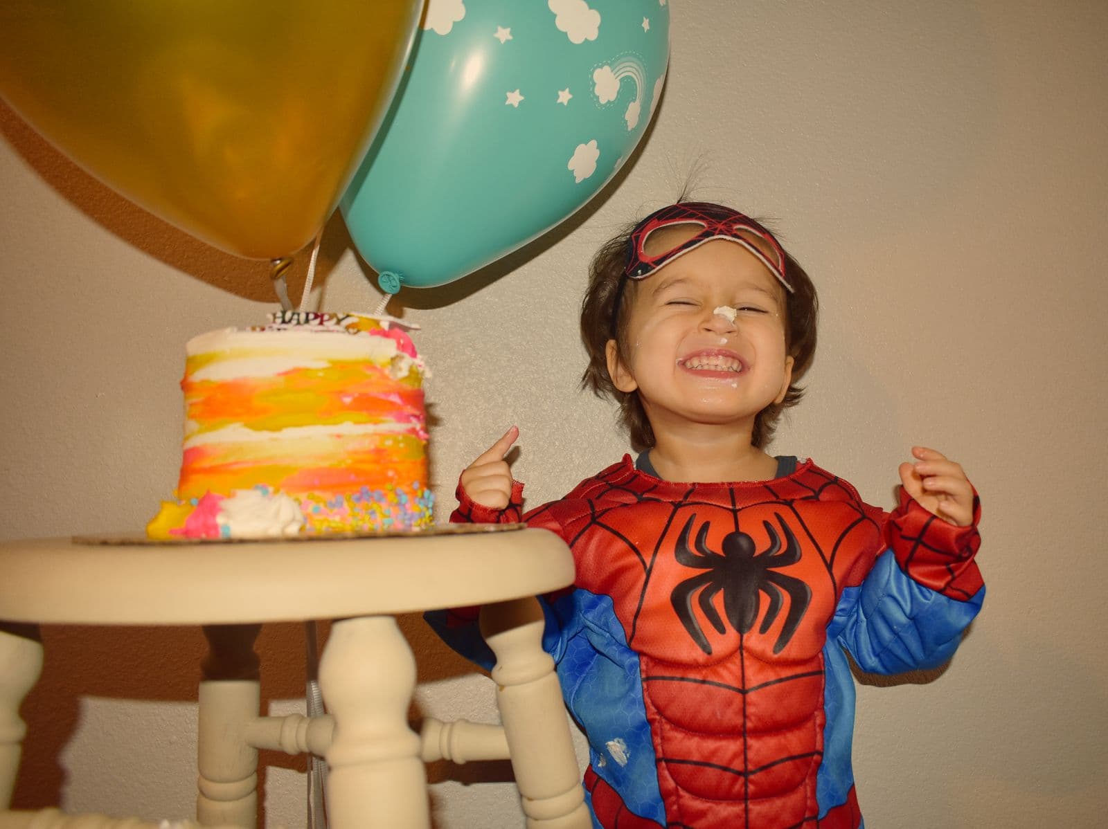 A boy in a superhero costume beside his birthday cake and balloons in Las Vegas, NV