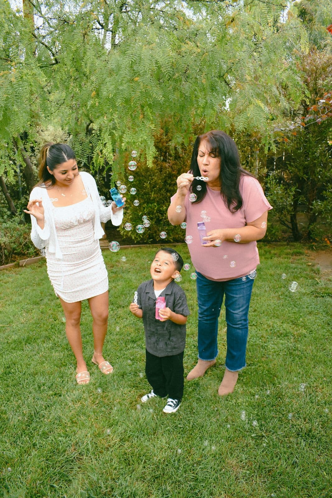 A family blowing bubbles with their toddler on a sunlit lawn during a Las Vegas, NV family session