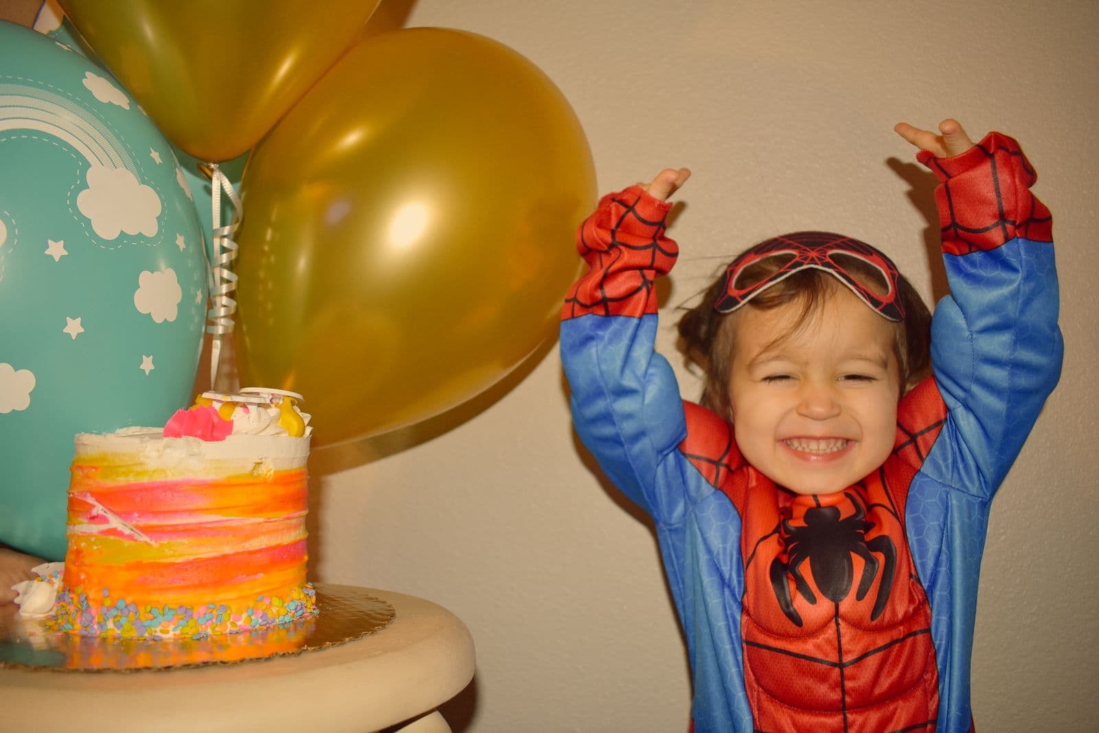 A boy in a superhero costume throwing his arms up beside his birthday cake, Las Vegas, NV