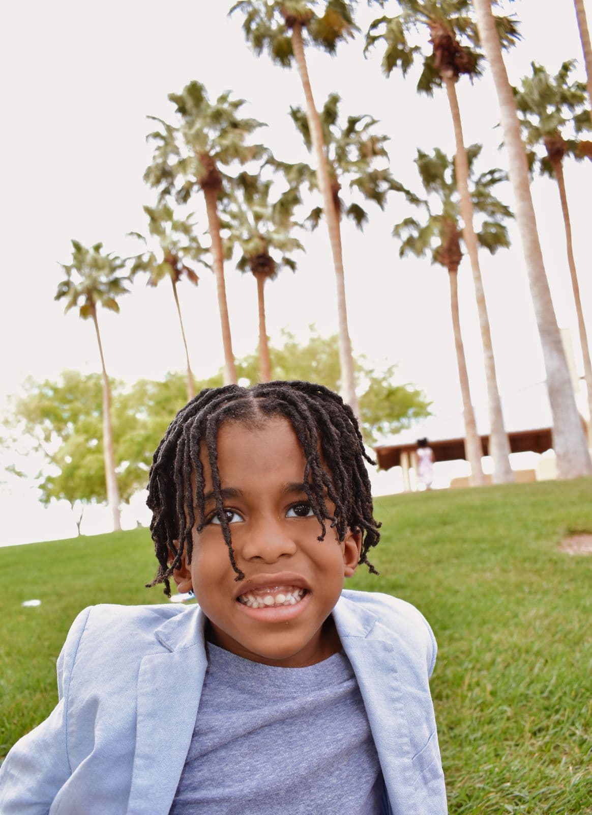 A young boy in a light blue blazer smiling on a park lawn during a family session in Las Vegas, NV