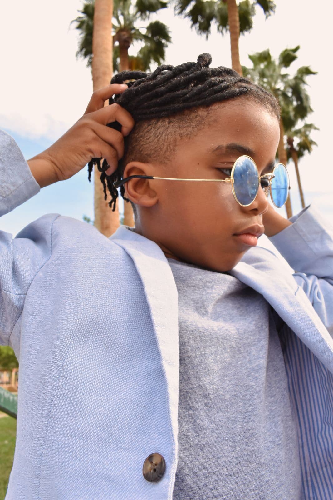 A boy in a blazer and round sunglasses having his hair straightened at a Las Vegas, NV park session