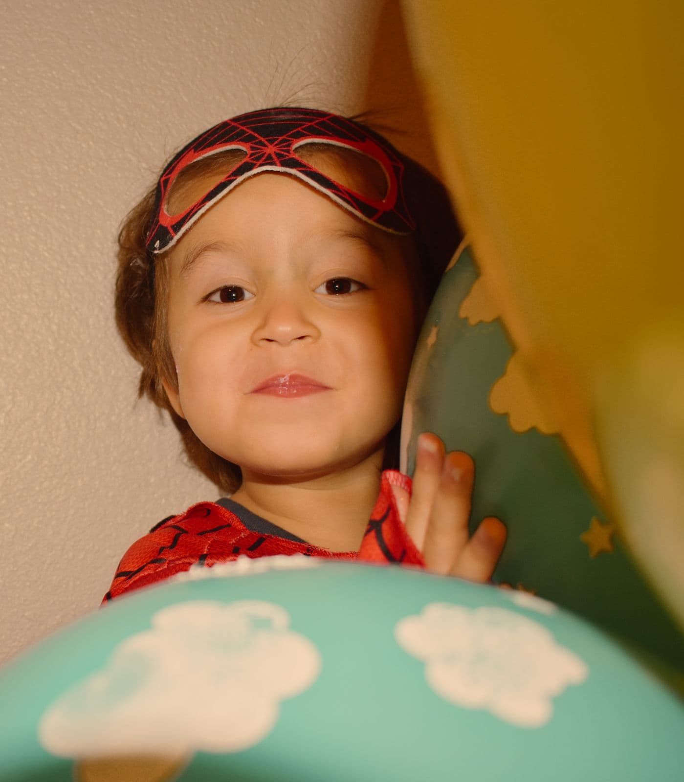 A young boy in a superhero costume peeking over a cloud-print balloon at his birthday, Las Vegas, NV