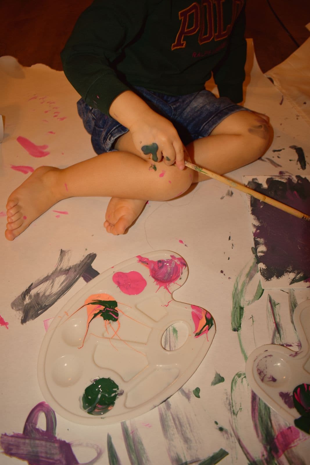 A child sitting on the floor beside a paint palette and brushes, Las Vegas, NV at-home session