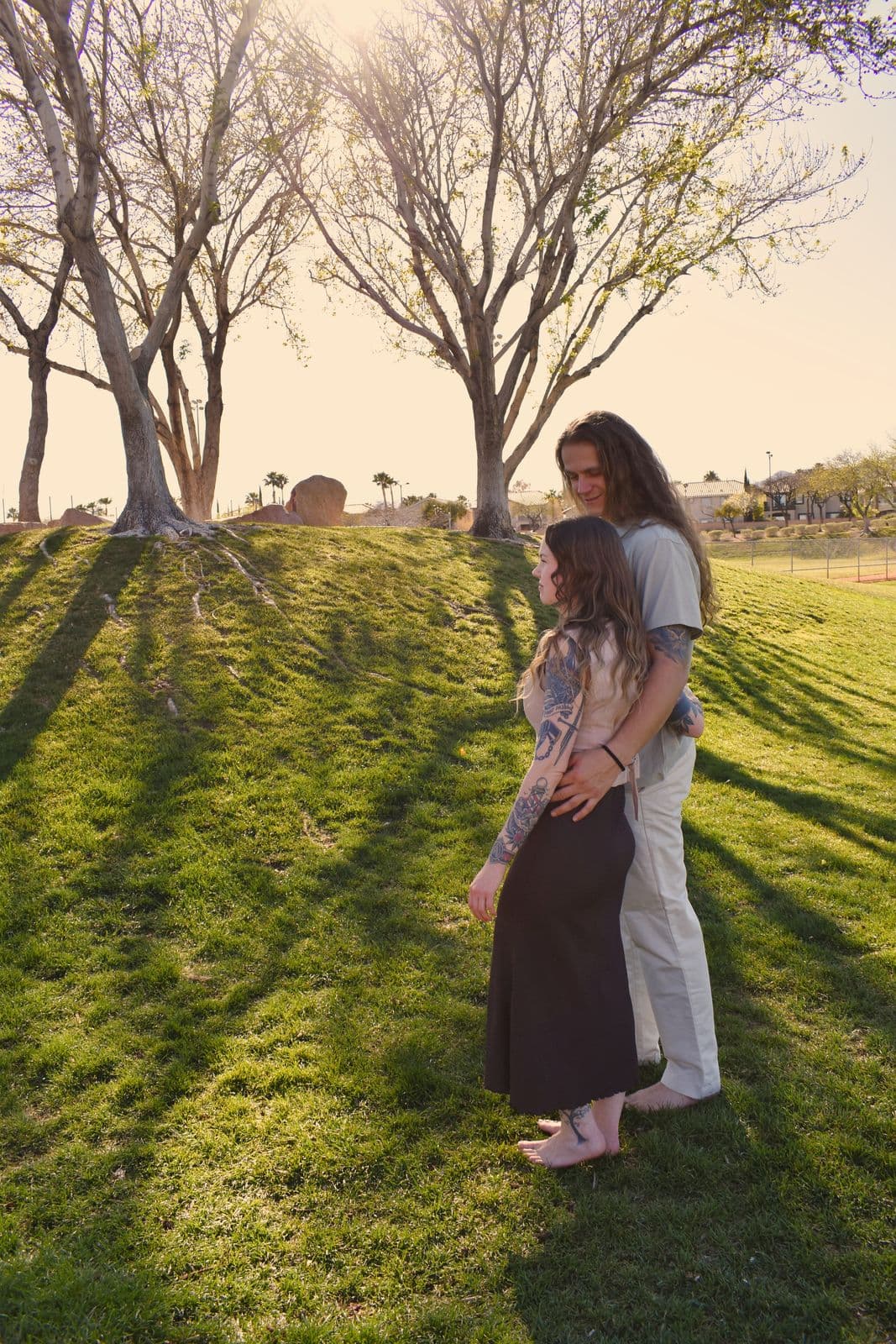 A couple standing together on a park lawn in low golden light during a family session in Las Vegas, NV