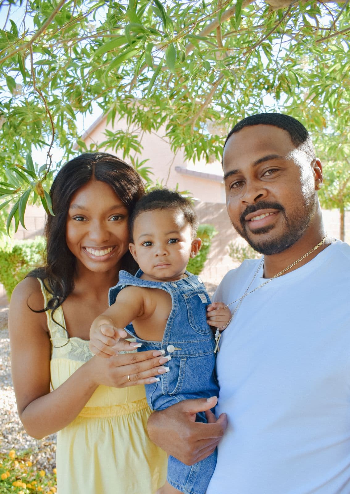 A mother, father and toddler photographed together under a leafy tree in Las Vegas, NV