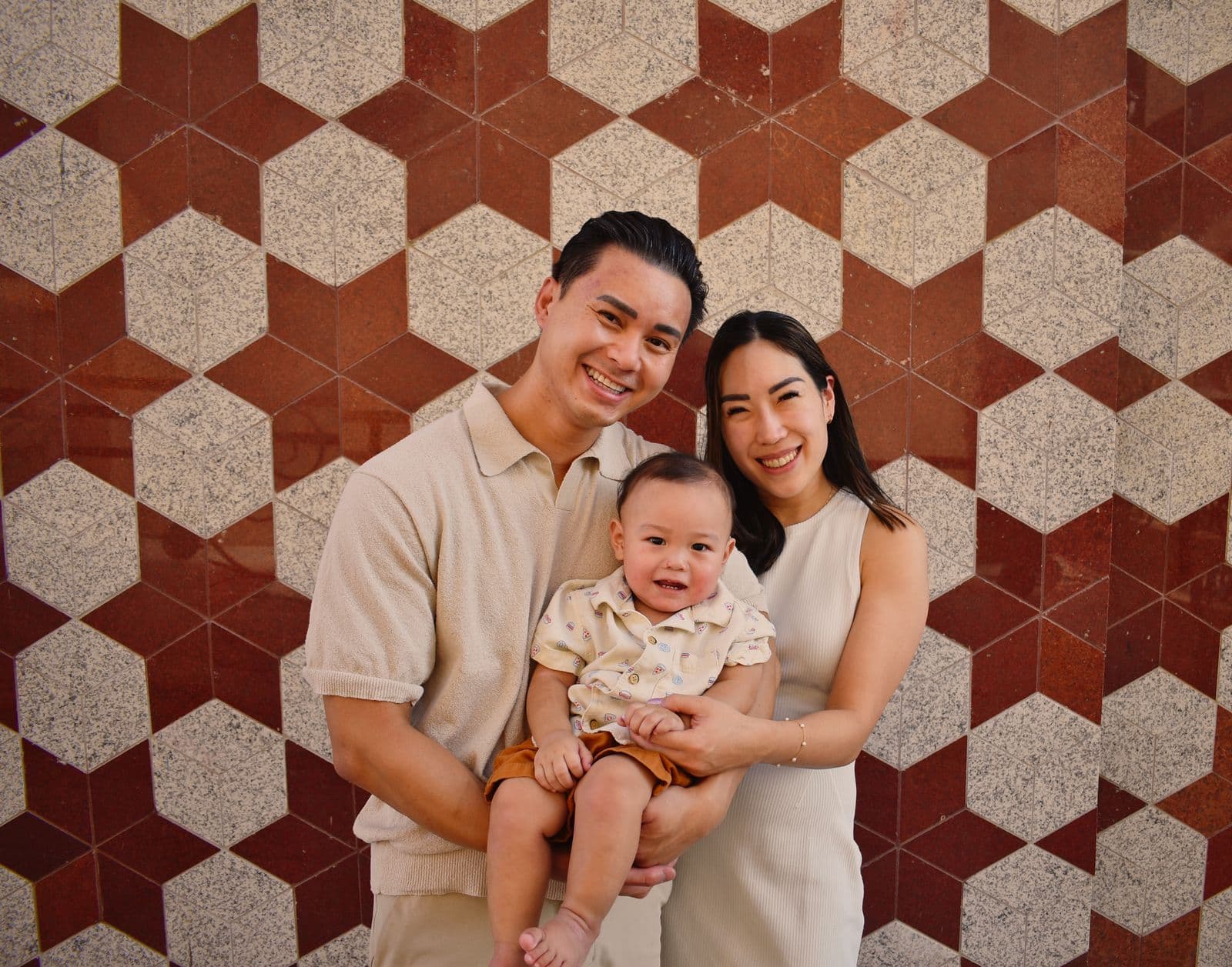 A family of three photographed against a red geometric tile wall in Las Vegas, NV