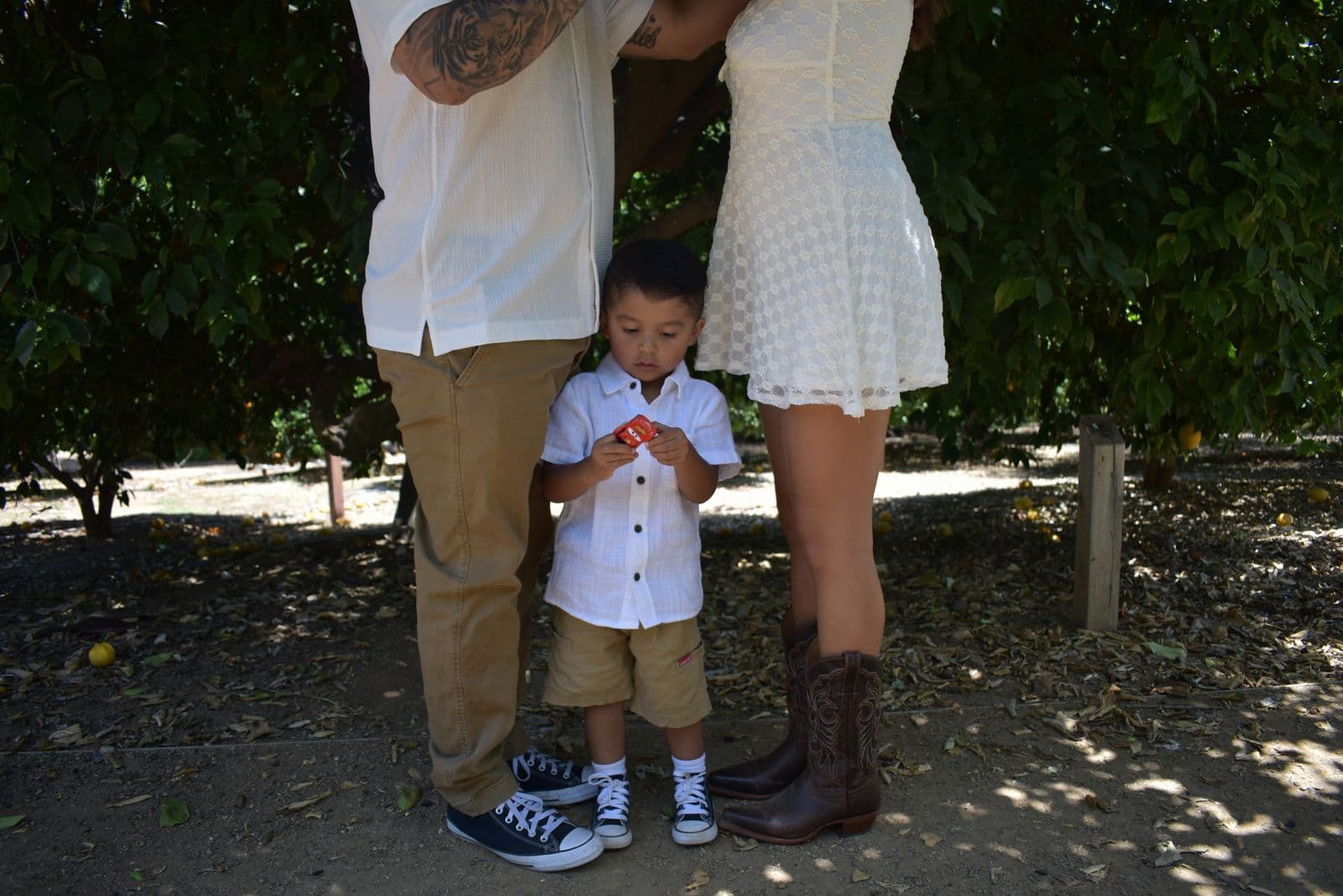 A family of three standing together in a sunlit orange grove during a Las Vegas, NV session