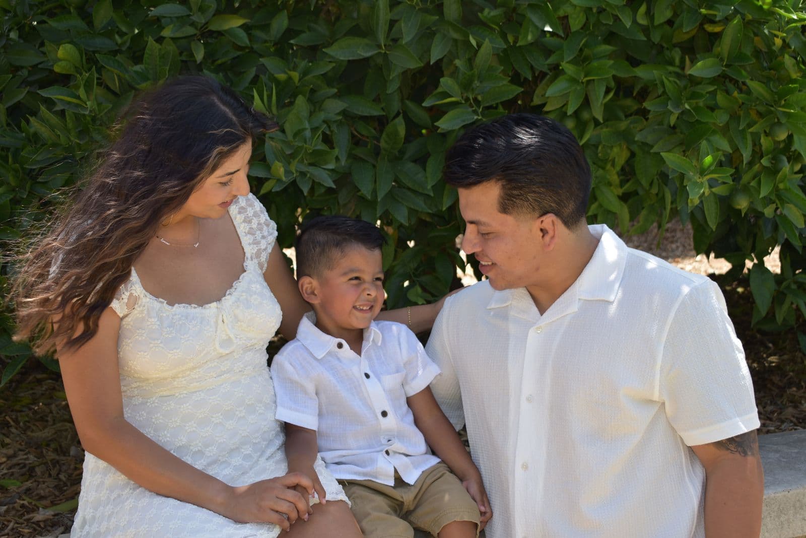 A family of three seated on a stone wall in front of a tall green hedge, Las Vegas, NV