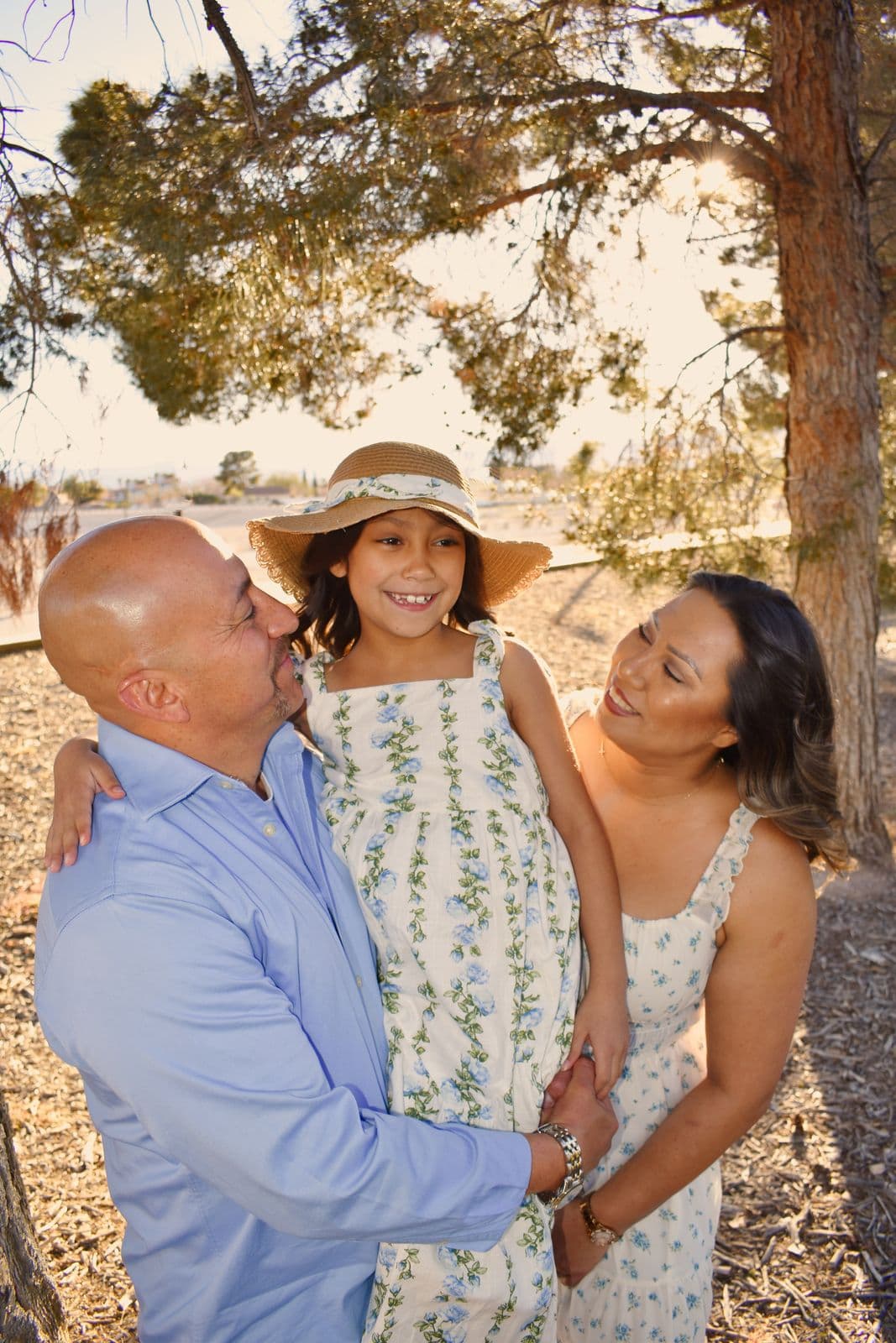 A family of three under a tree, their daughter in a straw hat between them, Las Vegas, NV