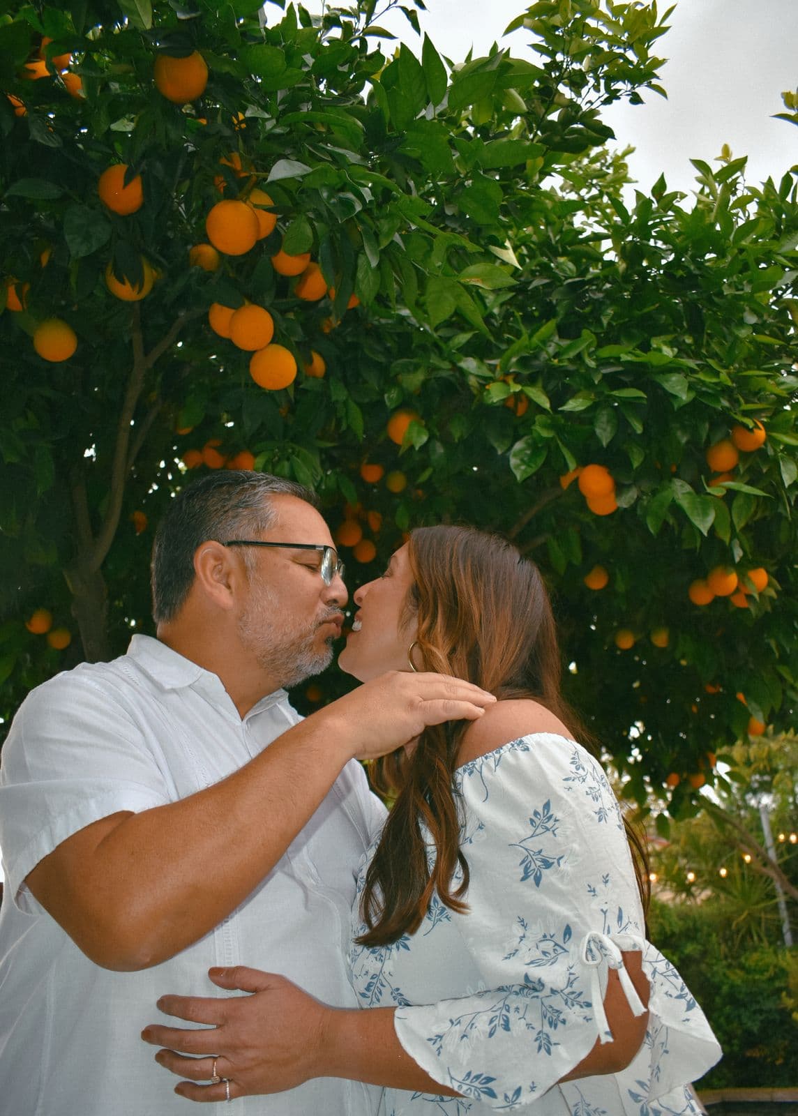A father kissing his daughter's forehead beneath a fruit-laden orange tree in Las Vegas, NV