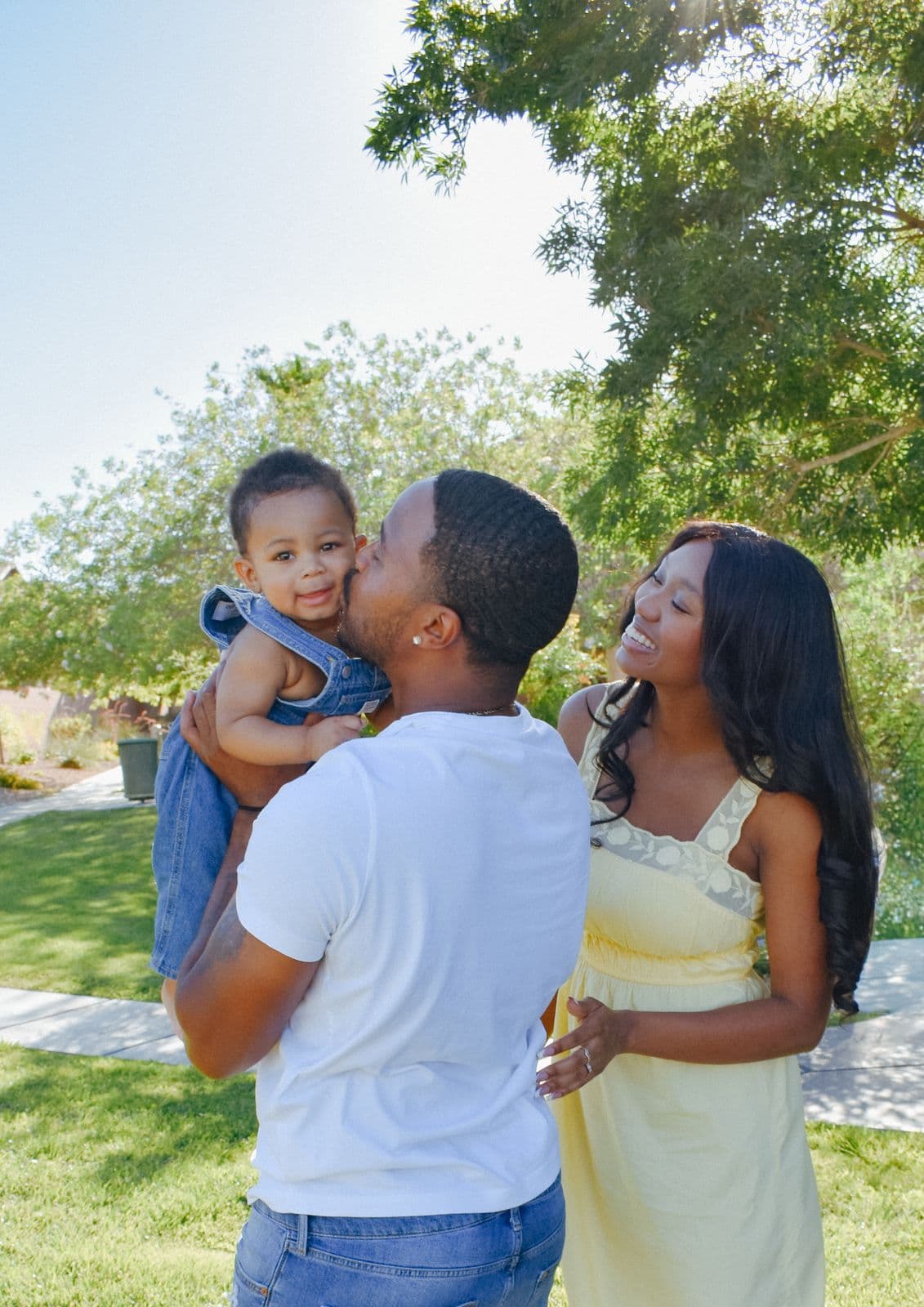 A father kissing his toddler on the cheek while her mother looks on during a Las Vegas, NV family session