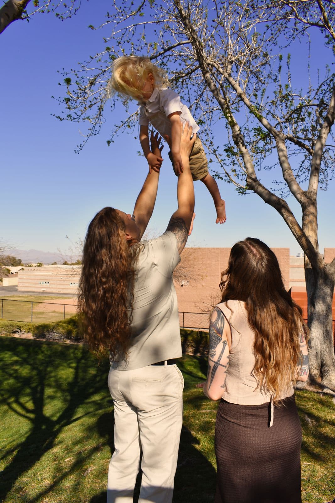 A father tossing his toddler into the air against a bright blue sky in Las Vegas, NV