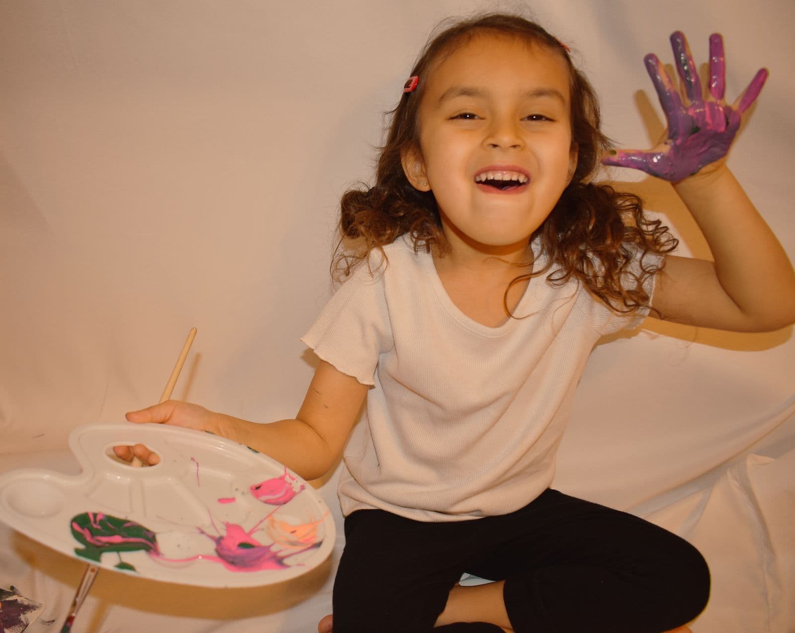 A young girl laughing and holding up a paint-covered hand during an at-home session in Las Vegas, NV