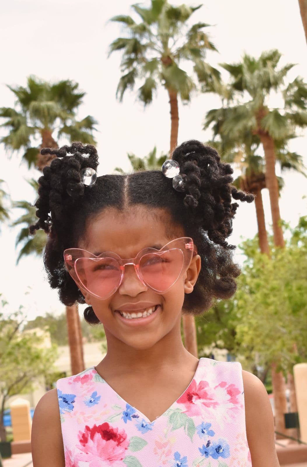 A young girl in pink heart-shaped sunglasses smiling during a family session in Las Vegas, NV