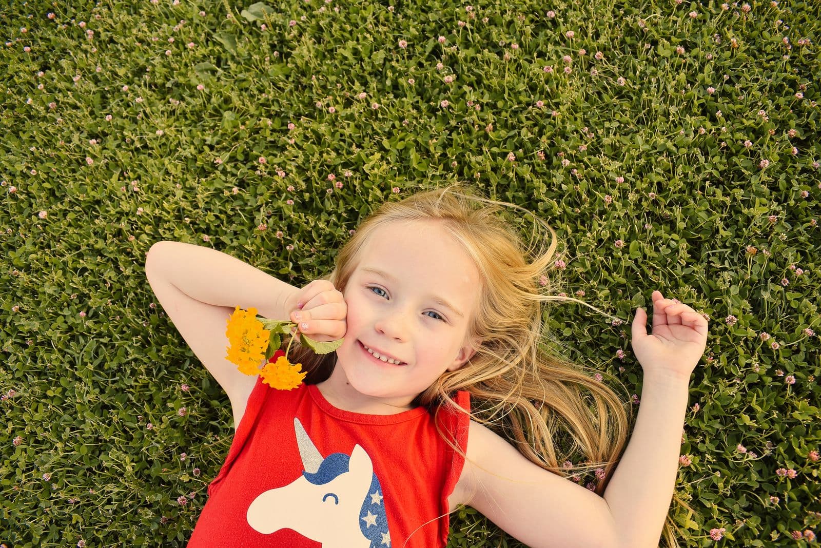 A girl in a red dress lying in the grass with a flower during a family session in Las Vegas, NV