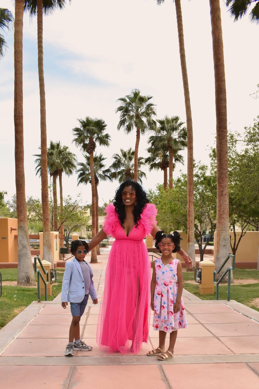A mother in a pink gown walking a palm-lined path with her son and daughter in Las Vegas, NV