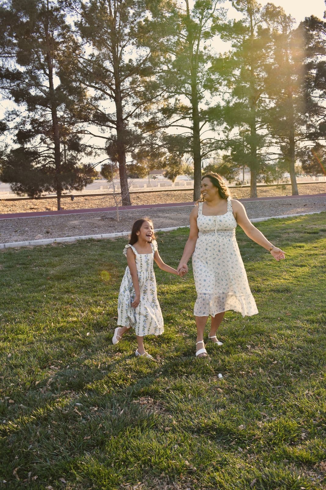 A mother and daughter holding hands as they walk across a park lawn in Las Vegas, NV