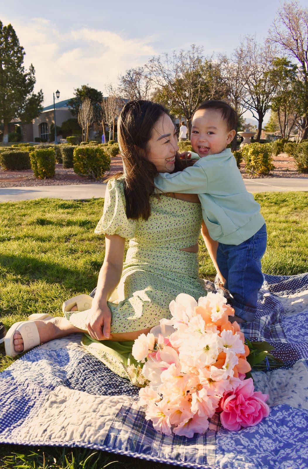 A mother hugging her toddler son from behind on a picnic blanket in a Las Vegas, NV park