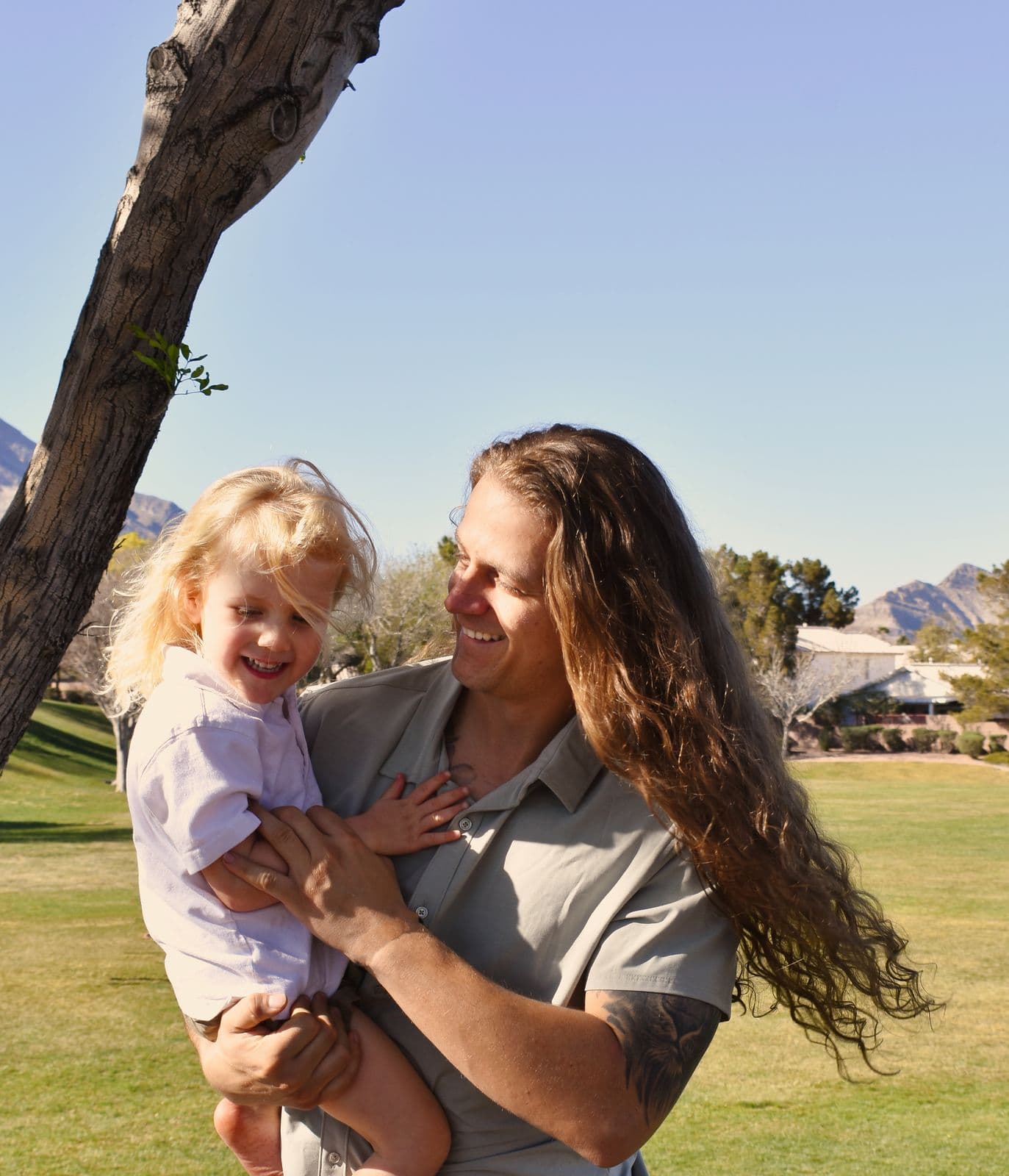 A mother lifting her laughing toddler on a green lawn during a family session in Las Vegas, NV