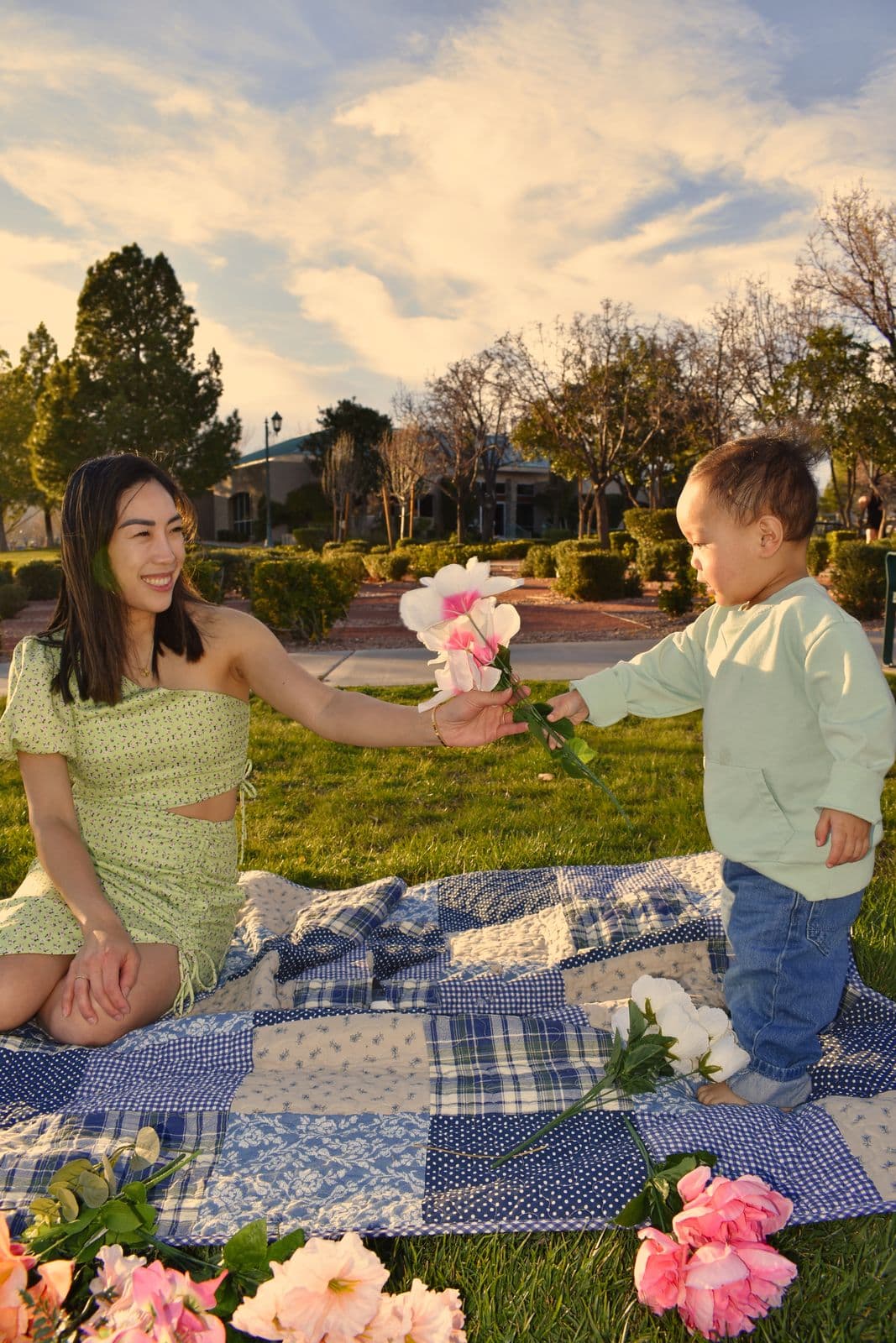 A mother kneeling on a patchwork picnic quilt offering flowers to her toddler, Las Vegas, NV