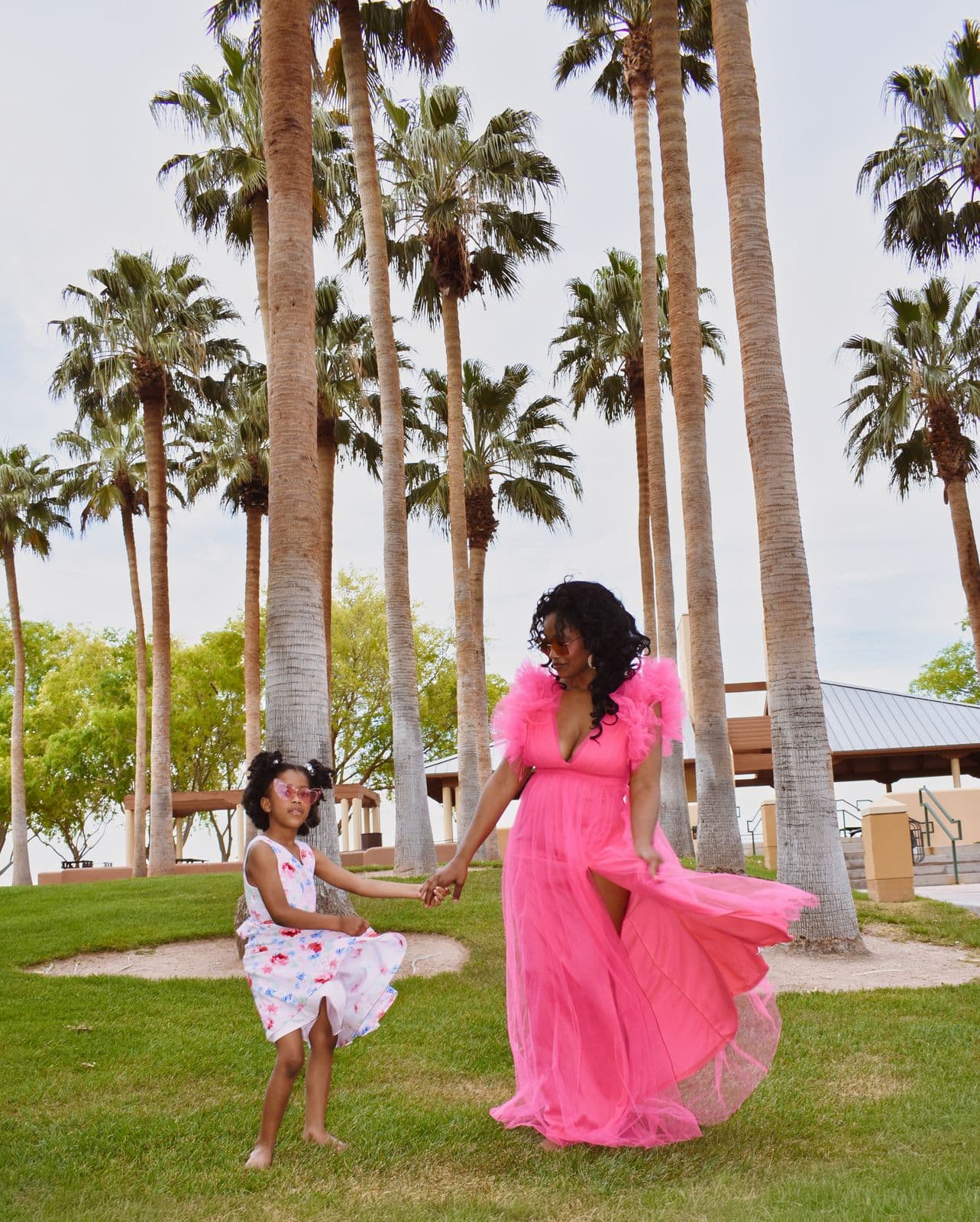 A mother in a flowing pink gown holding her daughter's hand beneath tall palms in Las Vegas, NV