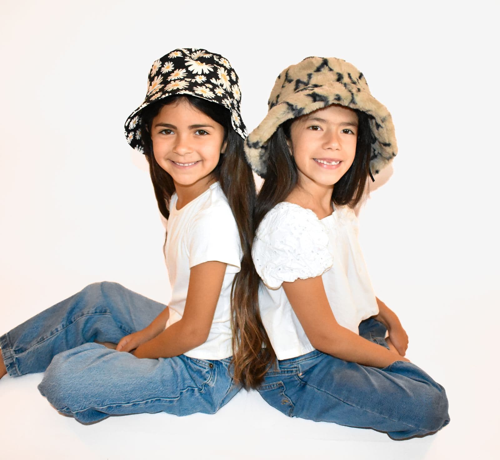 Two sisters in bucket hats sitting back to back during a studio sibling session in Las Vegas, NV