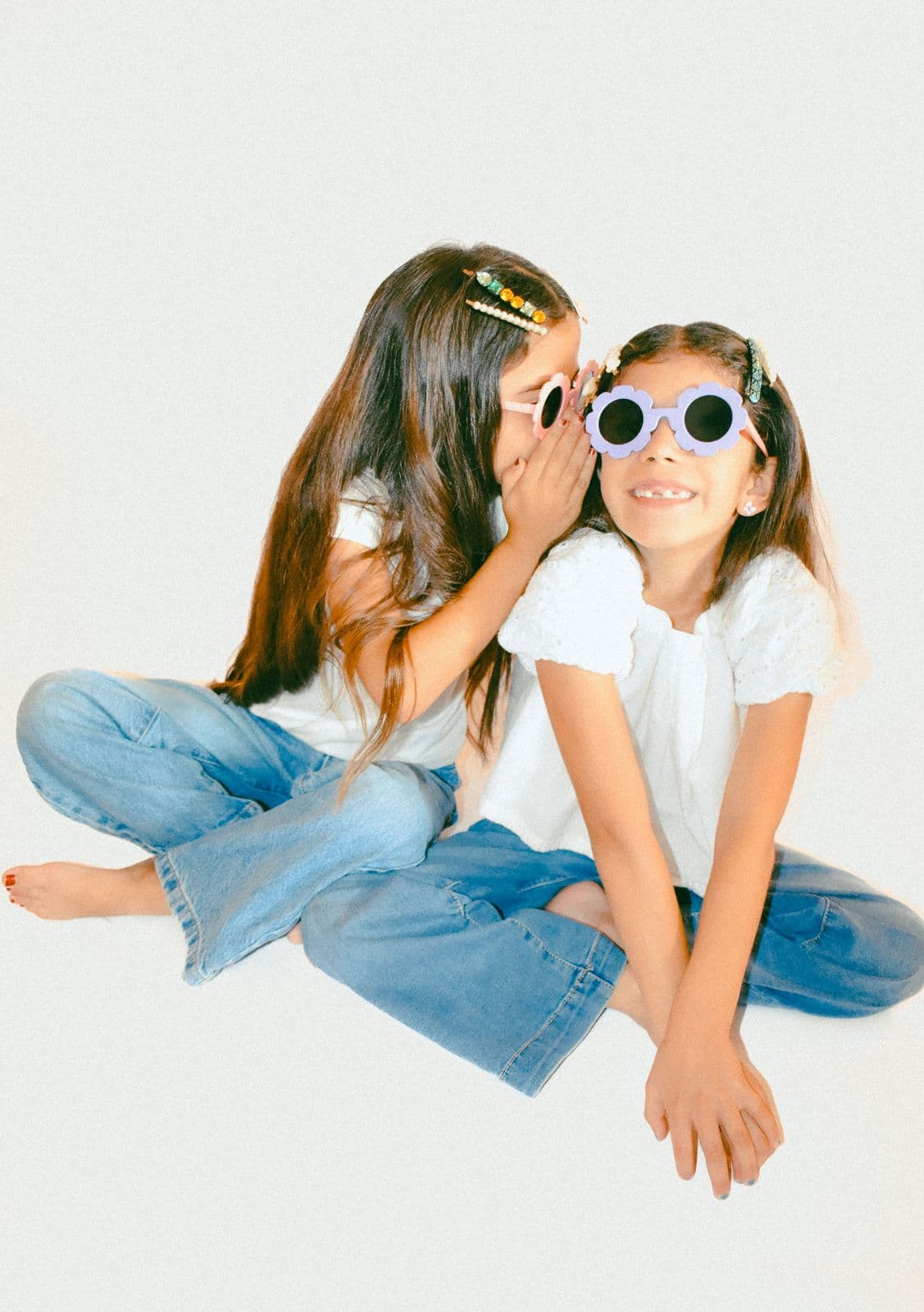 Two sisters seated on a studio floor, one adjusting the other's sunglasses, Las Vegas, NV
