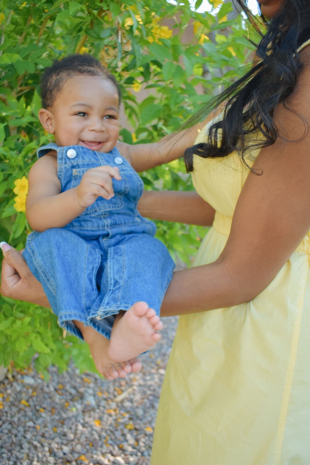 A laughing toddler in denim overalls held up by her mother during a family session in Las Vegas, NV