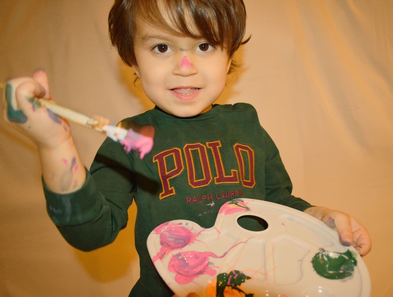 A toddler holding a paint palette and brush during an at-home family session in Las Vegas, NV