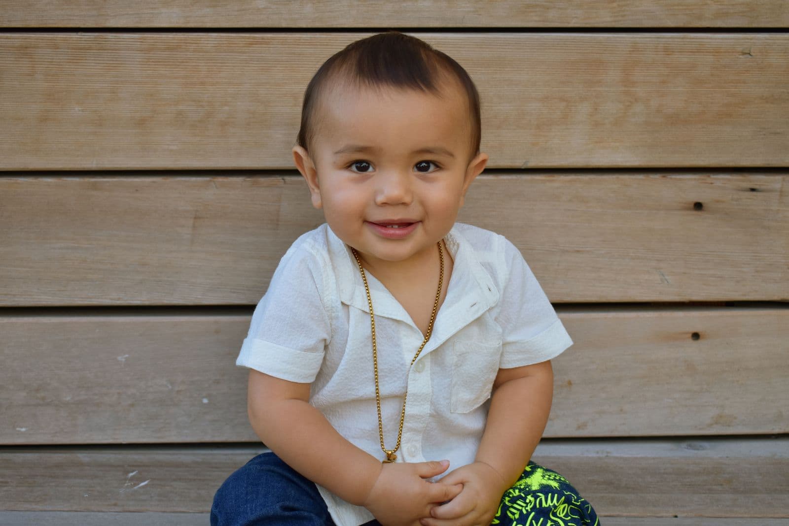 A toddler in a white shirt seated against a warm wooden wall in Las Vegas, NV