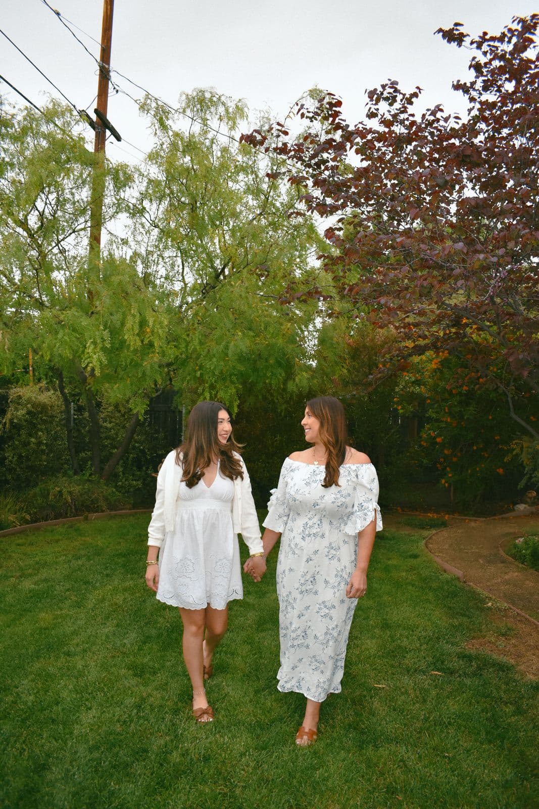 Two sisters in white dresses walking barefoot across a green lawn during a family session in Las Vegas, NV