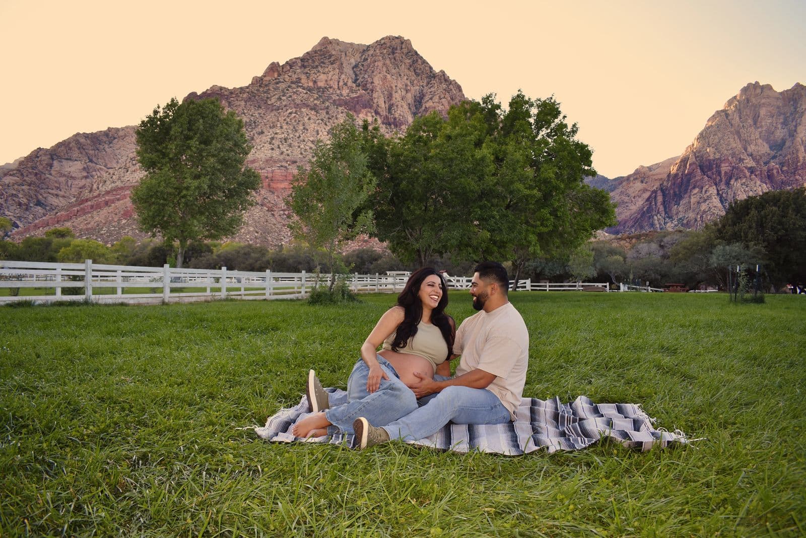 An expecting couple relaxing together on a striped blanket on the grass at Floyd Lamb Park in Las Vegas