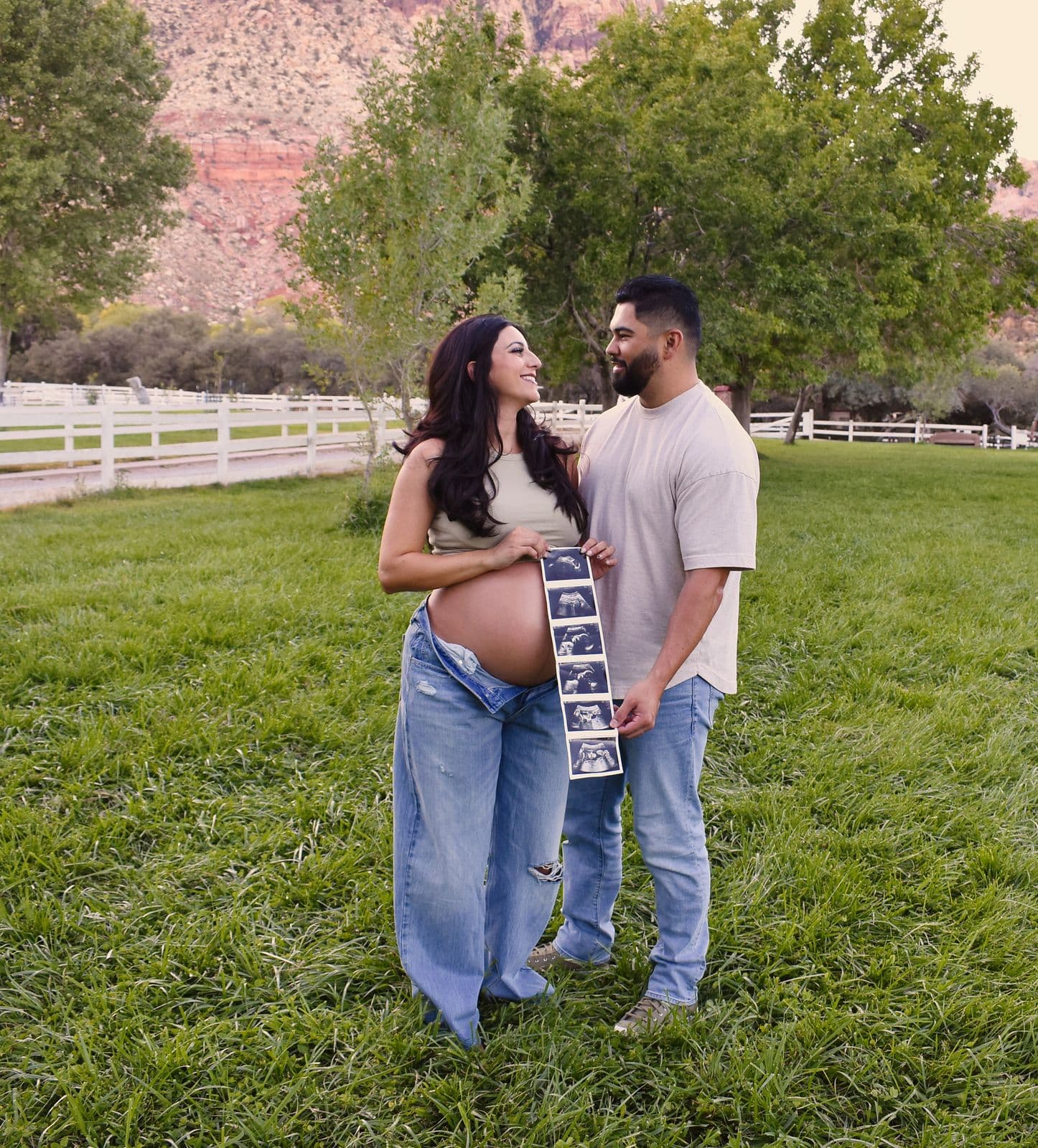 An expecting couple standing on the lawn at Floyd Lamb Park in Las Vegas, holding a strip of ultrasound photographs between them