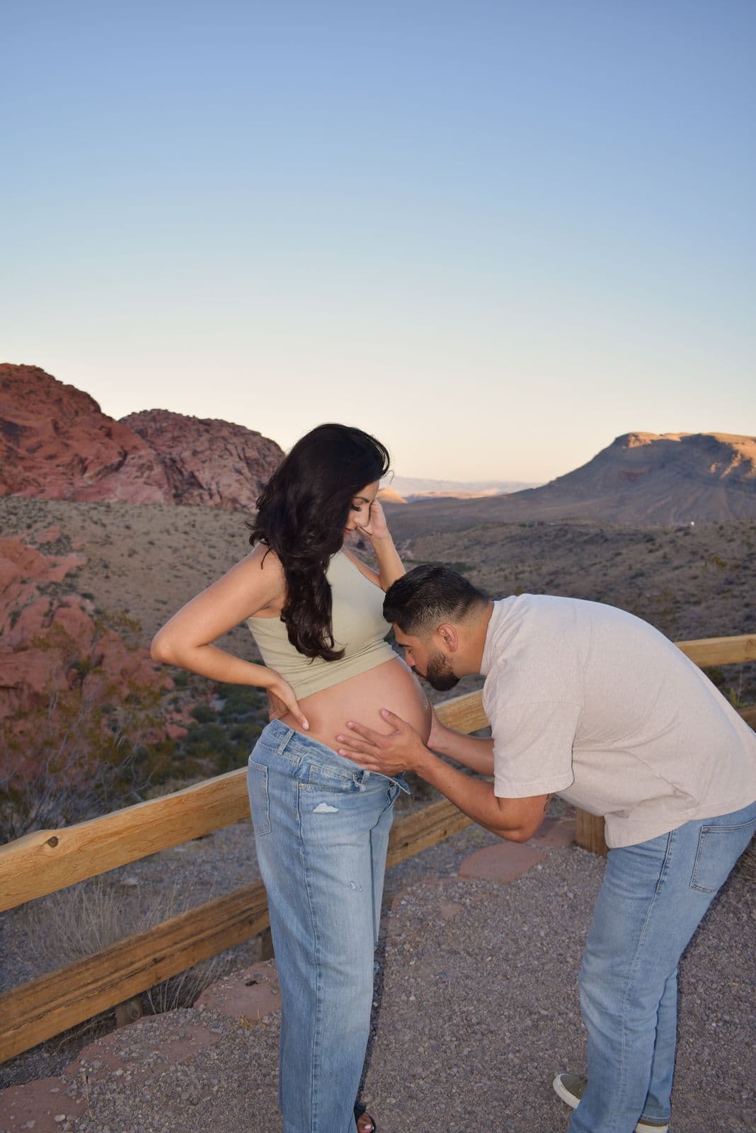 A partner bending to kiss an expecting mother's bare bump at an overlook on the Red Rock Canyon scenic drive near Las Vegas