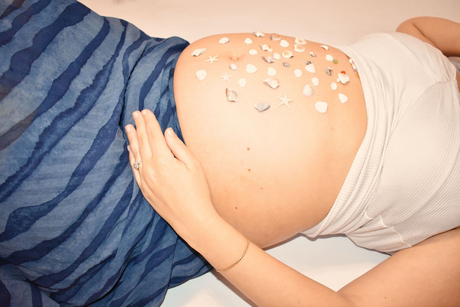 Overhead close-up of an expecting mother's bump scattered with small white flower petals during a Las Vegas studio maternity session
