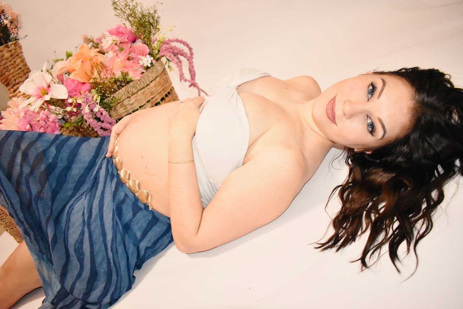 An expecting mother lying on her side on a studio floor in Las Vegas in a blue draped skirt, looking toward the camera