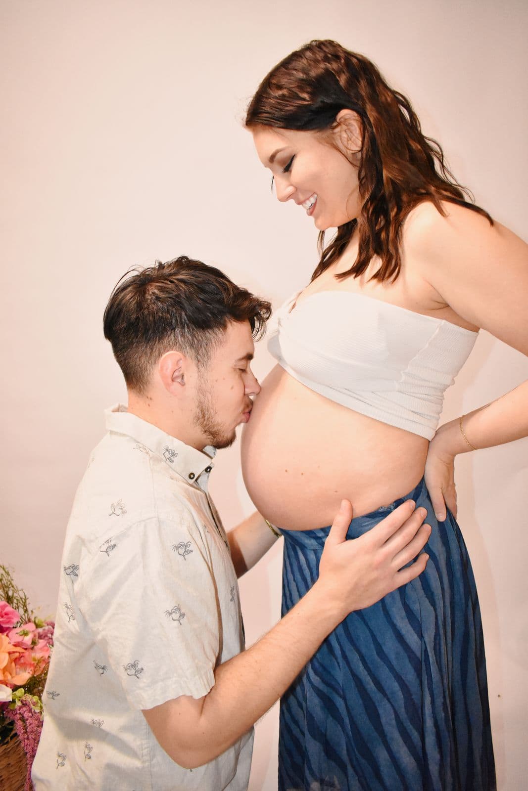 A partner crouching to kiss an expecting mother's bare belly during an in-studio maternity session in Las Vegas