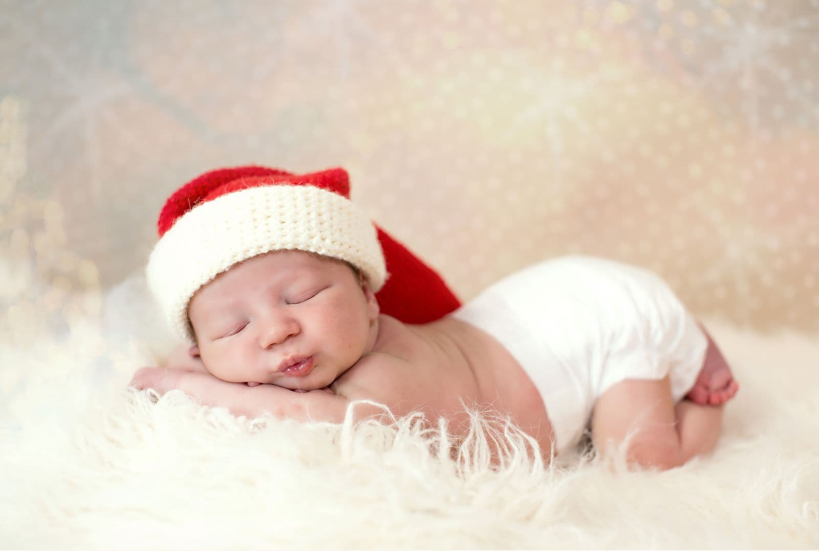 A newborn asleep on a white fur blanket in a red and cream stocking cap during an in-studio newborn session in Las Vegas, NV