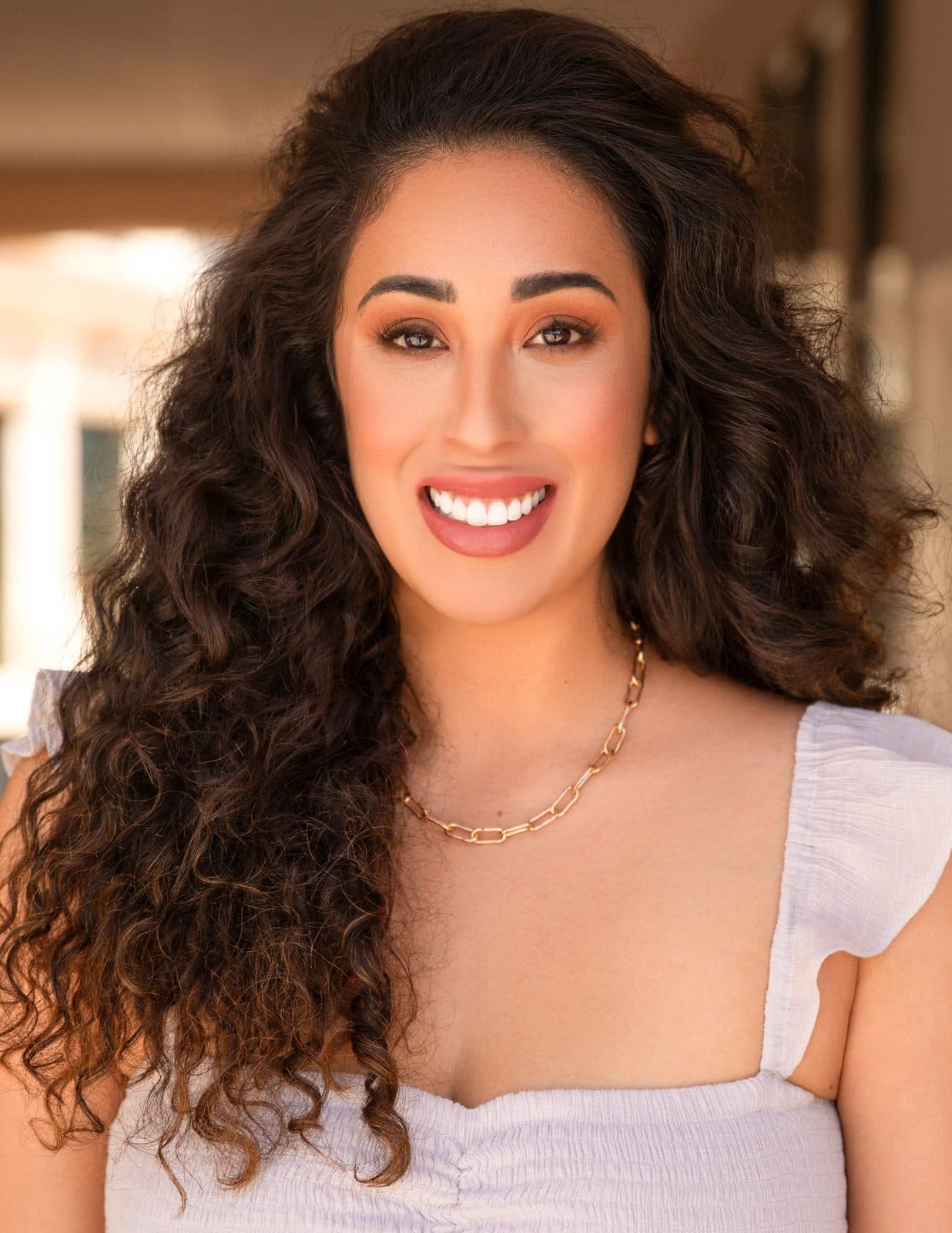 Melyssa Silva, the Las Vegas newborn, maternity and family photographer behind Silva Studios Photography, smiling in a white top with long dark curly hair